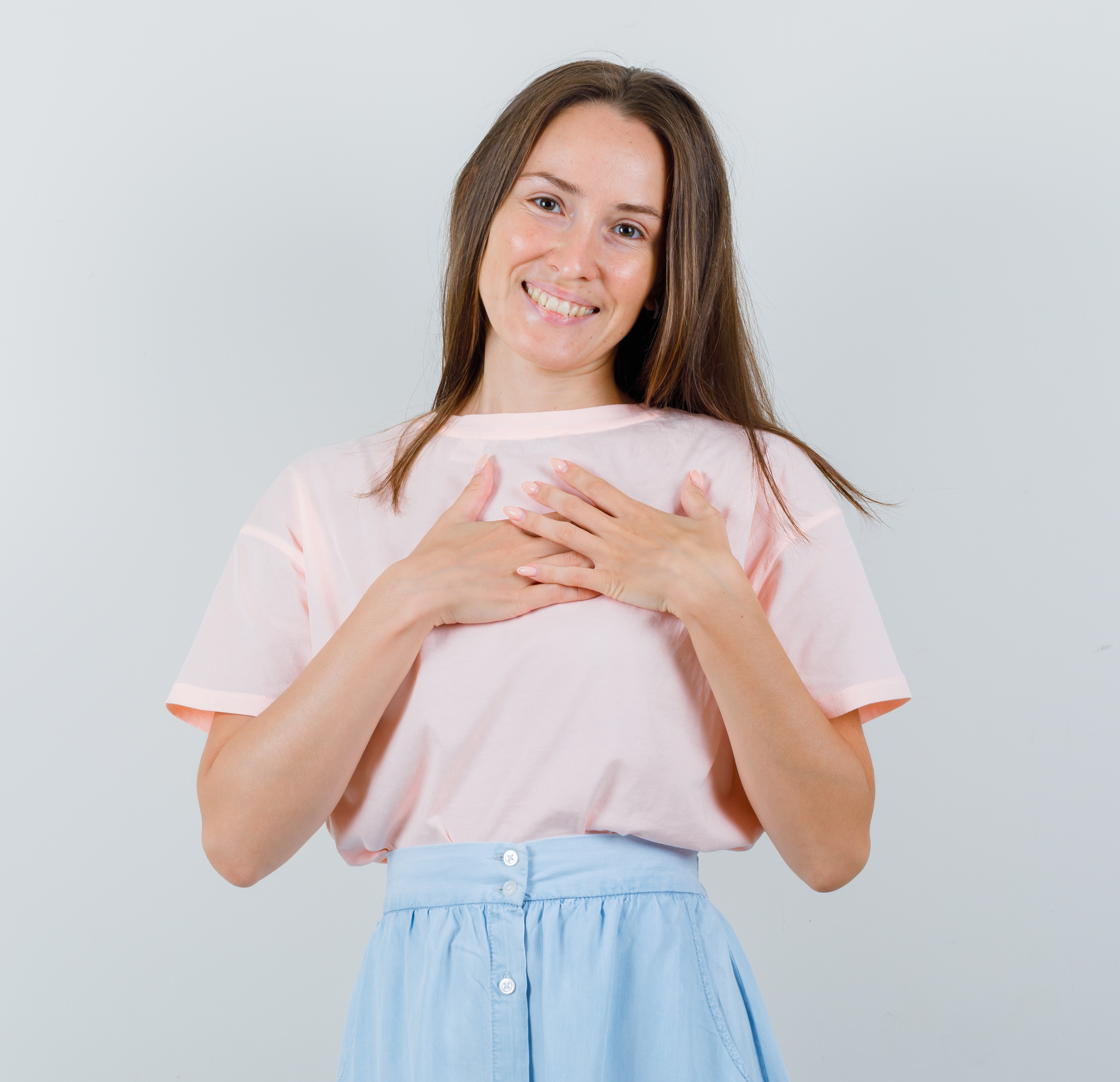 Young girl holding hands on heart in t-shirt, skirt and looking cheerful. front view.
